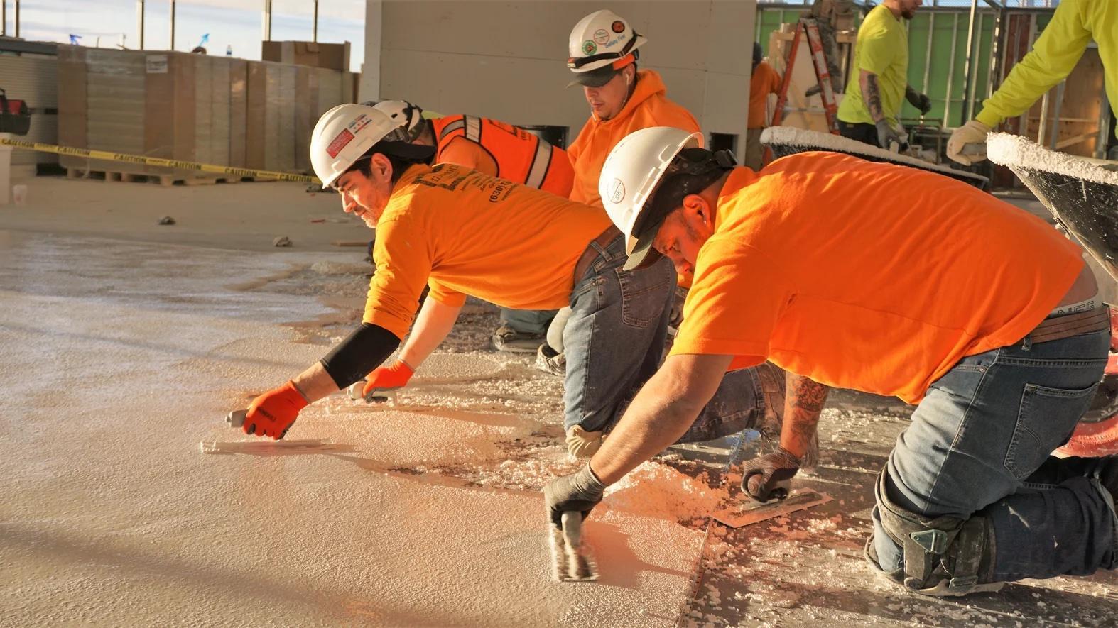 Multiple people wearing hardhats applying tile adhesive on a floor